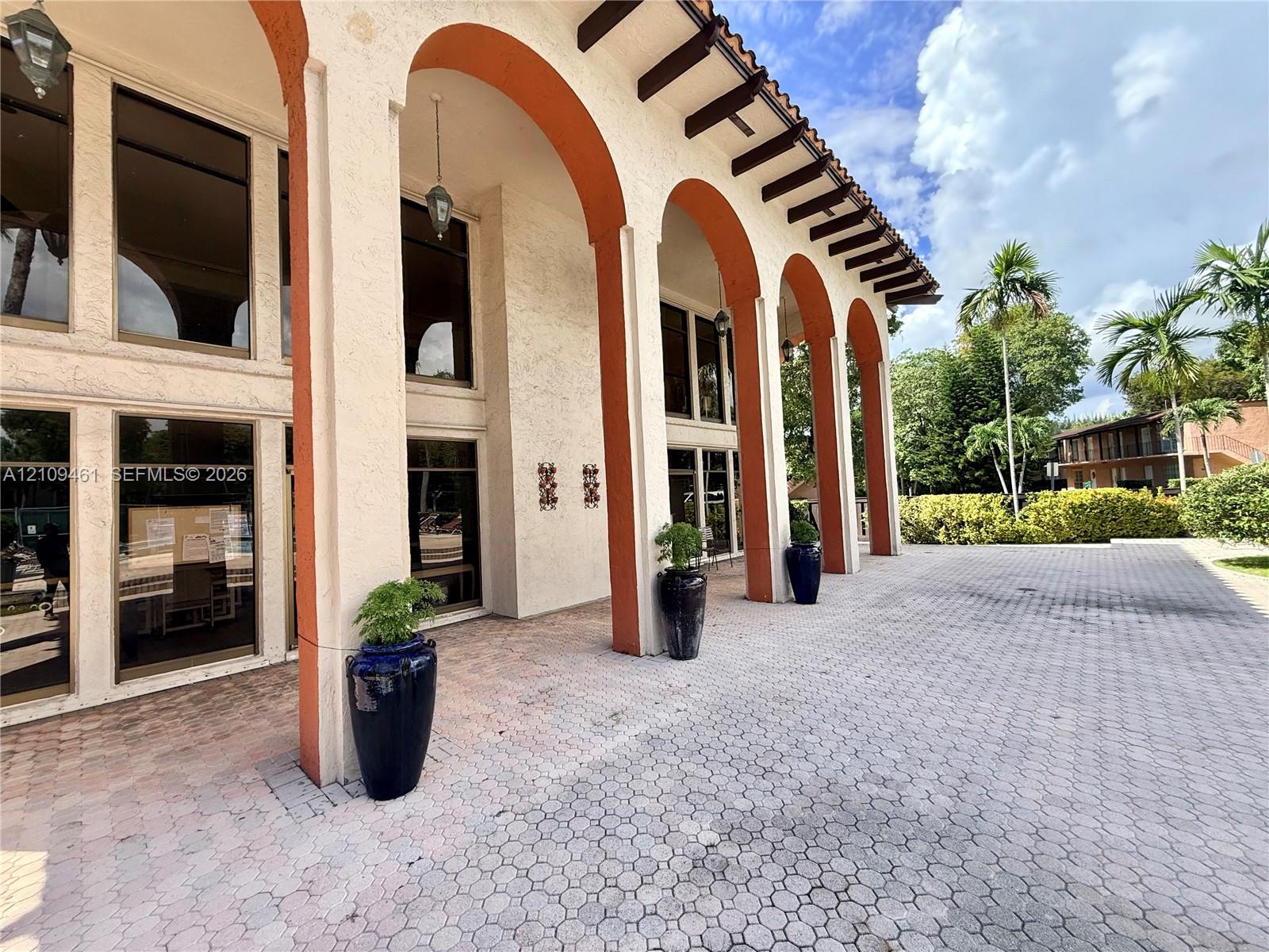 Stucco exterior featuring decorative arched colonnades, multi-pane floor-to-ceiling windows, exposed timber rafters, and a paved stone courtyard