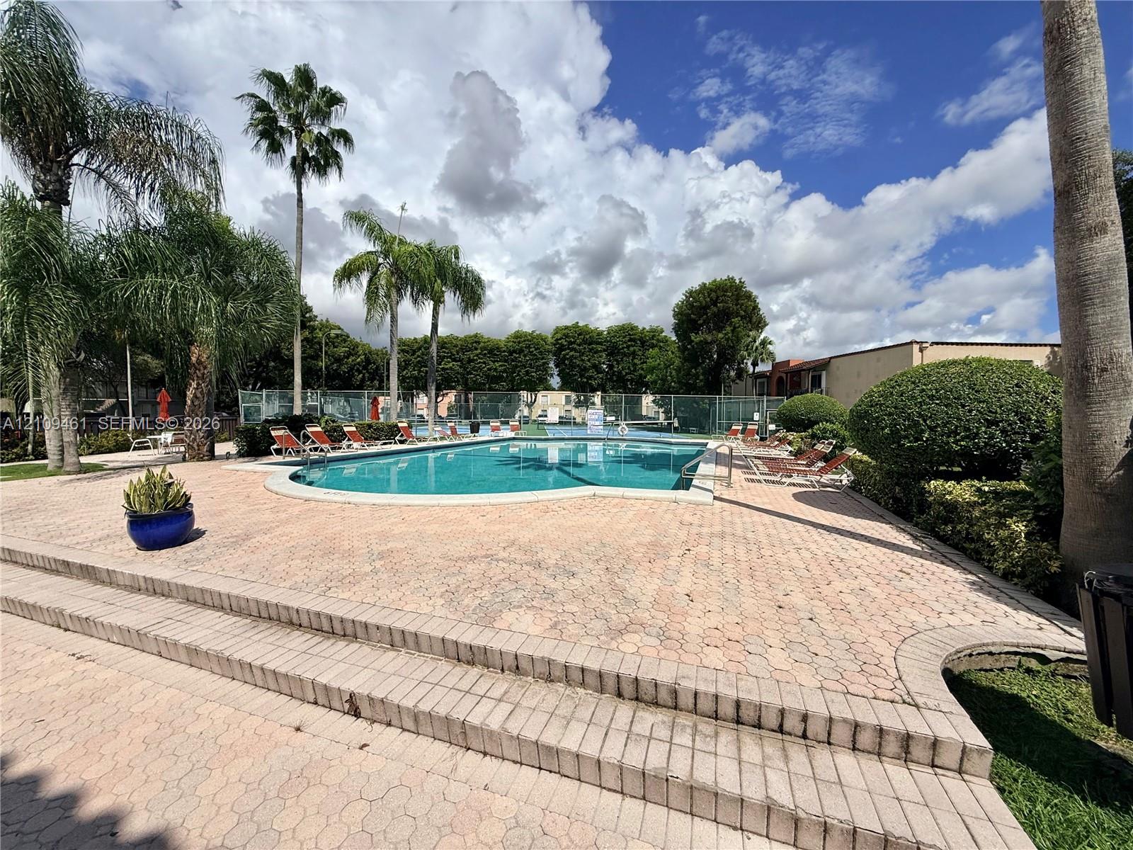 In-ground swimming pool featuring paver decking, multi-level stairs, and mature palm trees