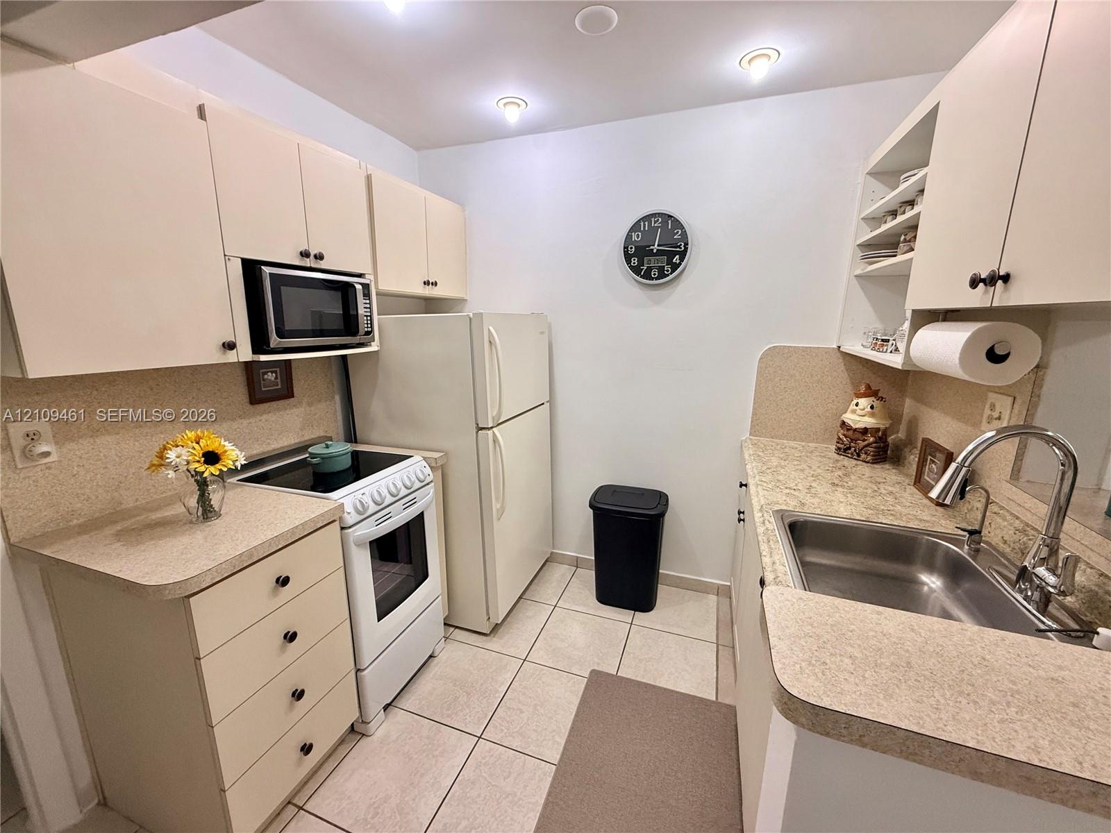 Kitchen featuring cabinetry with integrated storage, solid-surface countertops, stainless steel sink with high-arc faucet, and tiled flooring