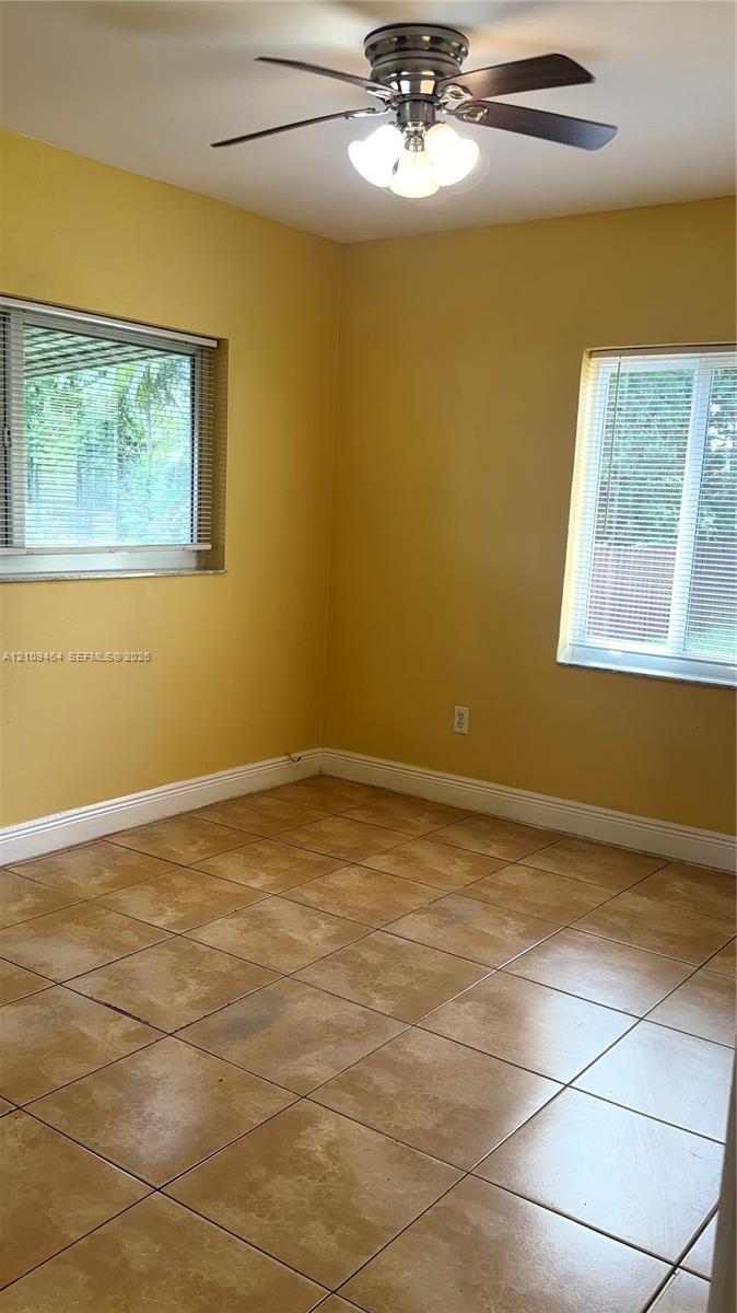 Room interior featuring neutral tile flooring, two windows with horizontal blinds, and a multi-light ceiling fan
