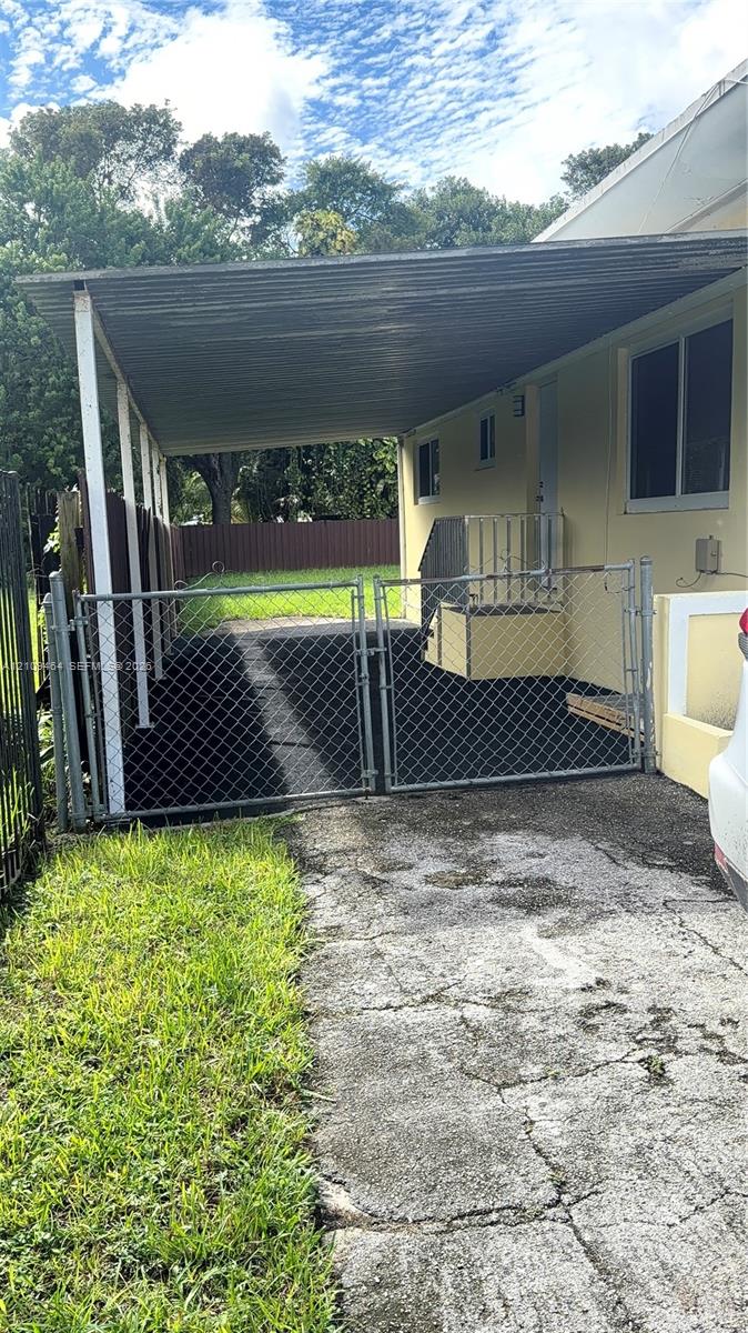 Covered carport with metal roof, enclosed side yard with chain-link fencing, dual-gate entry, and concrete driveway