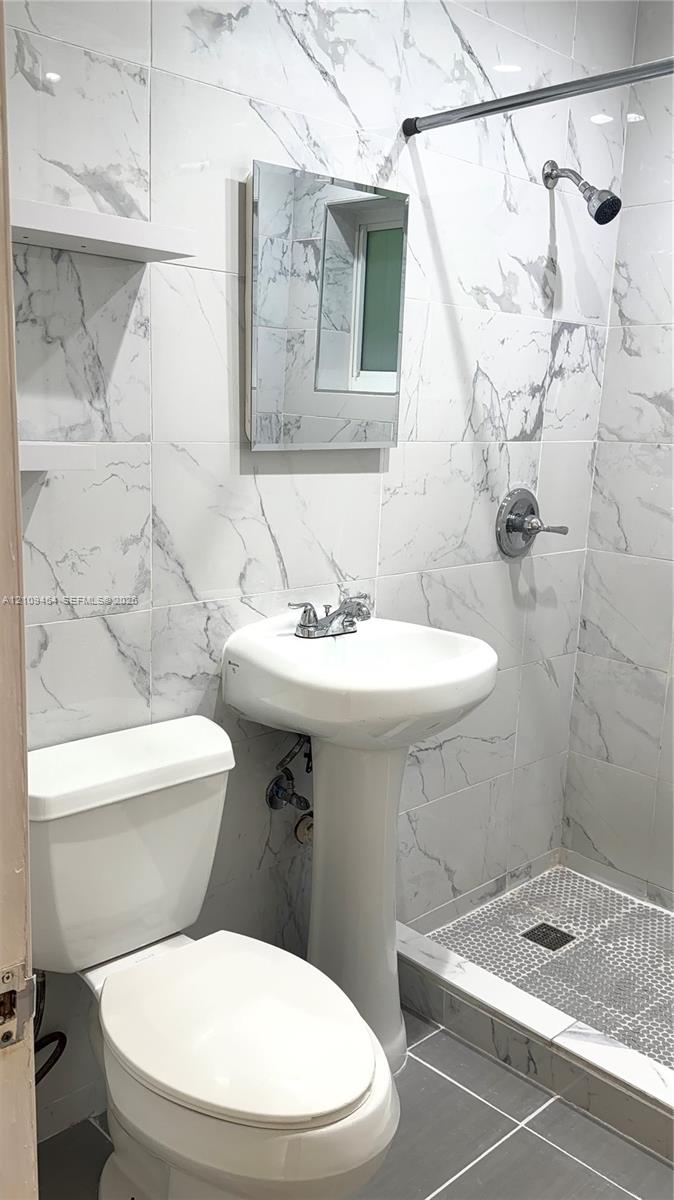 Full-height stone-finish wall tile, pedestal sink, wall-mounted medicine cabinet, built-in shelving, and walk-in shower with tiled flooring