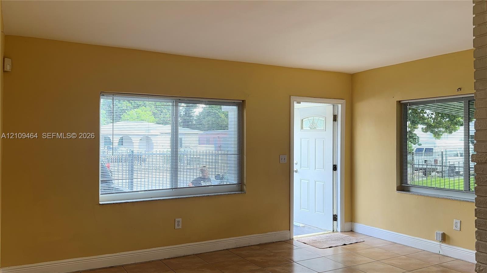 Interior space featuring tile flooring, two horizontal sliding windows with blinds, a white-paneled exterior door, and exposed masonry pillar detailing