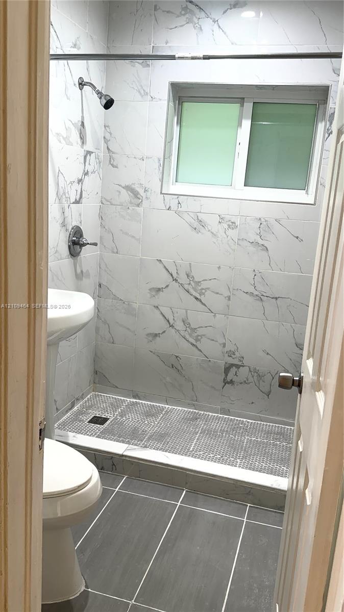 Walk-in shower featuring floor-to-ceiling stone-look tile, a mosaic-tiled shower floor, a white pedestal sink, and large-format grey tile flooring