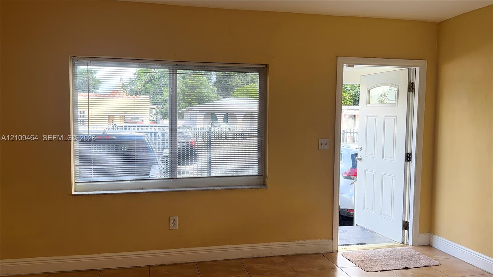 Large dual-pane sliding window, exterior door with inset glass panel, and neutral tile flooring