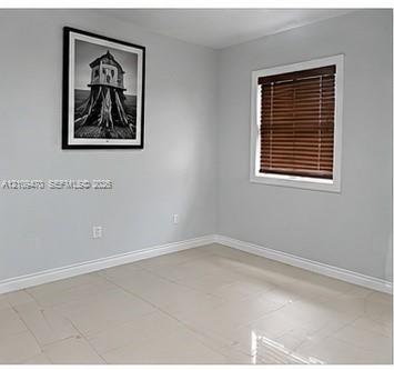 Neutral-toned interior space featuring light-colored tile flooring, smooth wall finishes, and a window equipped with brown horizontal blinds