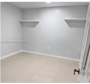 Room featuring neutral-toned tile flooring, light gray walls, and dual built-in wall-mounted shelves