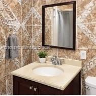 Vanity featuring a stone-composite countertop, undermount sink, dual-handle faucet, and dark wood-finish cabinetry, complemented by patterned ceramic wall tile and a framed mirror