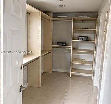 Walk-in closet featuring light-toned custom shelving, multiple hanging rods, and large-format tile flooring
