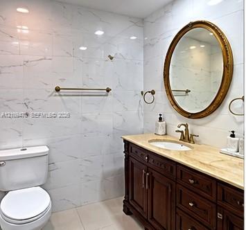 Bathroom vanity featuring a natural stone countertop, undermount sink, dark wood-finish cabinetry, and an oval mirror, complemented by floor-to-ceiling wall tiling and gold-toned fixtures Bathroom vanity featuring a natural stone countertop, undermount sink, dark wood-finish cabinetry, and an oval mirror, complemented by floor-to-ceiling wall tiling and gold-toned fixtures