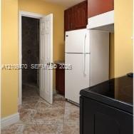 Kitchen featuring dark-toned cabinetry, a white refrigerator, black stovetop, and patterned tile flooring Kitchen featuring dark-toned cabinetry, a white refrigerator, black stovetop, and patterned tile flooring