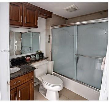 Bathroom featuring wood-finish cabinetry, stone-surface countertop with an integrated oval sink, and a shower-tub combination with sliding glass doors