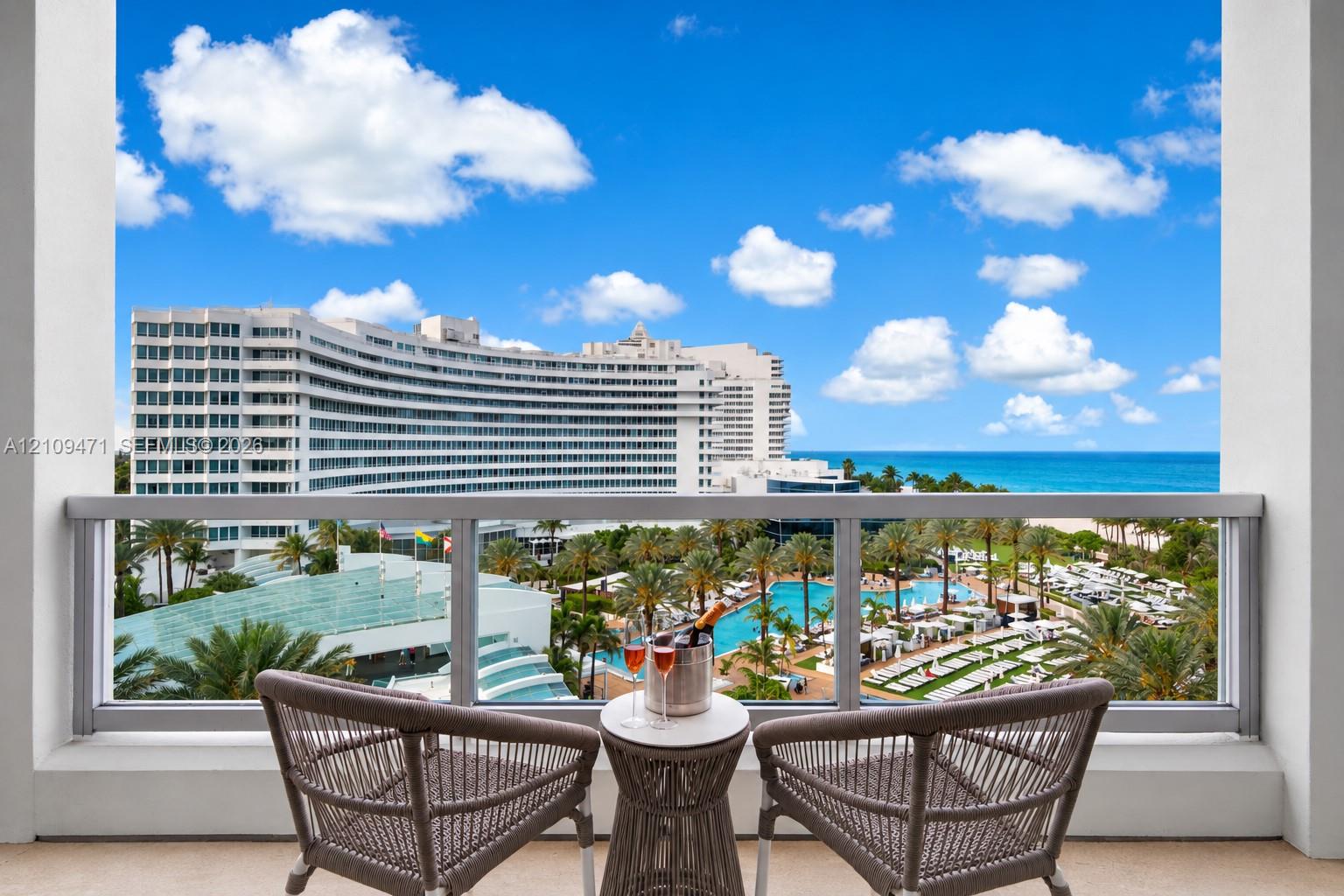 Covered balcony featuring a metal and glass railing, providing an elevated outlook over the ocean, sandy coastline, resort-style pools, and palm-lined grounds Covered balcony featuring a metal and glass railing, providing an elevated outlook over the ocean, sandy coastline, resort-style pools, and palm-lined grounds