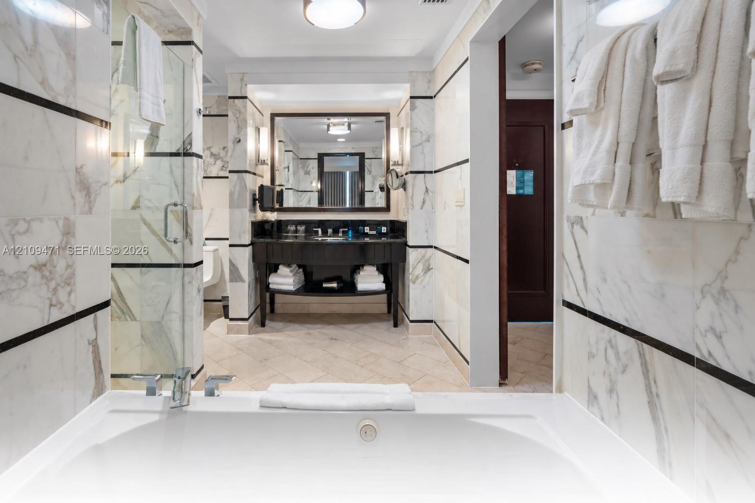 Stone-surround soaking tub, glass-enclosed shower, stone-tiled walls with decorative inlay, dark-finish vanity with countertop sink, and recessed lighting Stone-surround soaking tub, glass-enclosed shower, stone-tiled walls with decorative inlay, dark-finish vanity with countertop sink, and recessed lighting