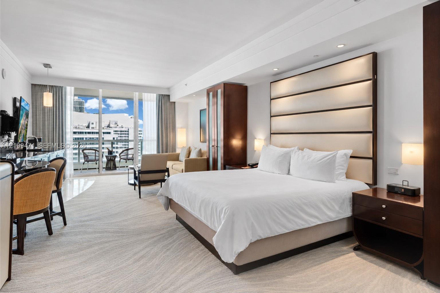 Full-height upholstered headboard featuring integrated lighting, custom dark-finish wood cabinetry, floor-to-ceiling glass sliding doors, and private balcony Full-height upholstered headboard featuring integrated lighting, custom dark-finish wood cabinetry, floor-to-ceiling glass sliding doors, and private balcony