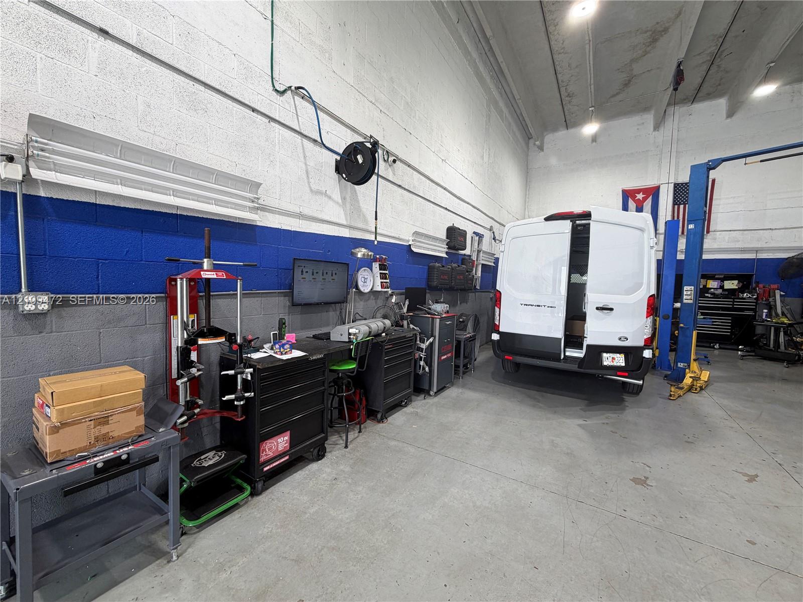 Industrial workspace featuring high ceilings, concrete flooring, painted masonry walls, and a built-in automotive lift