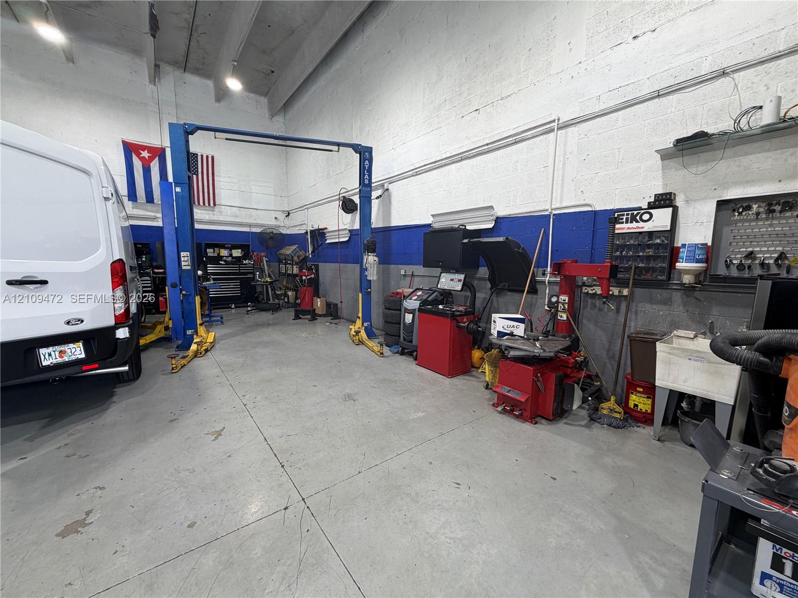 Industrial workspace featuring high-clearance concrete block walls, durable concrete flooring, a dual-post automotive lift, and an integrated utility basin