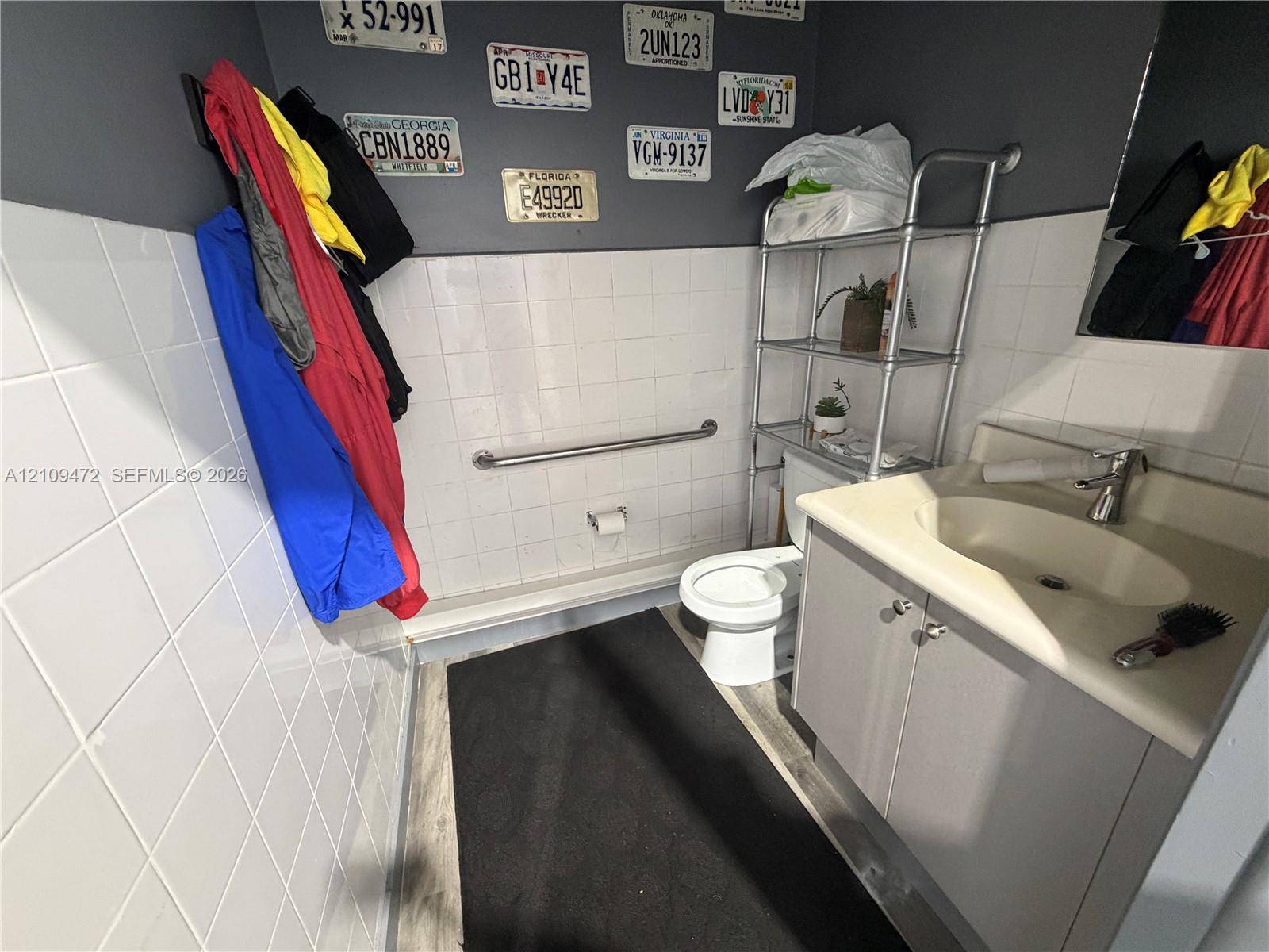 Vanity featuring a molded sink basin and gray cabinetry, white wall tile, horizontal grab bar, and wood-finish flooring