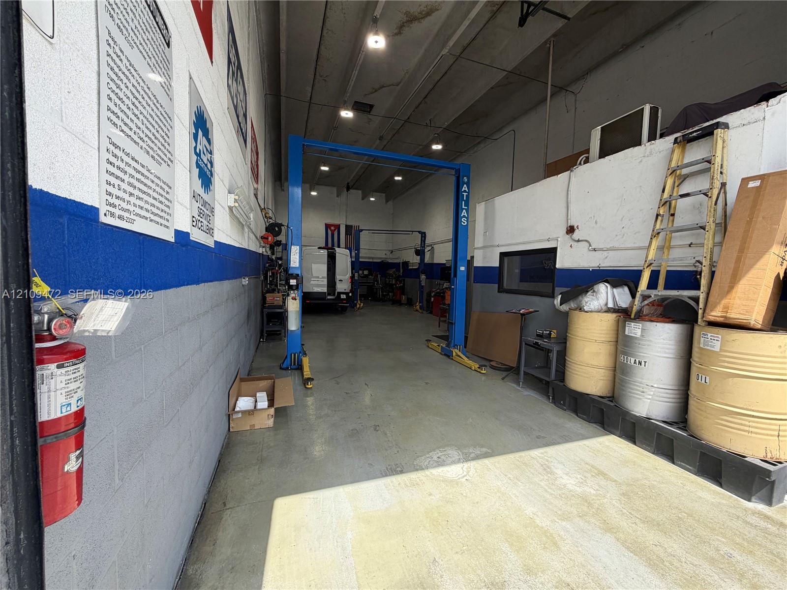 Industrial garage space featuring painted masonry walls, high-clearance ceilings with recessed lighting, integrated two-post automotive lift, and smooth concrete flooring
