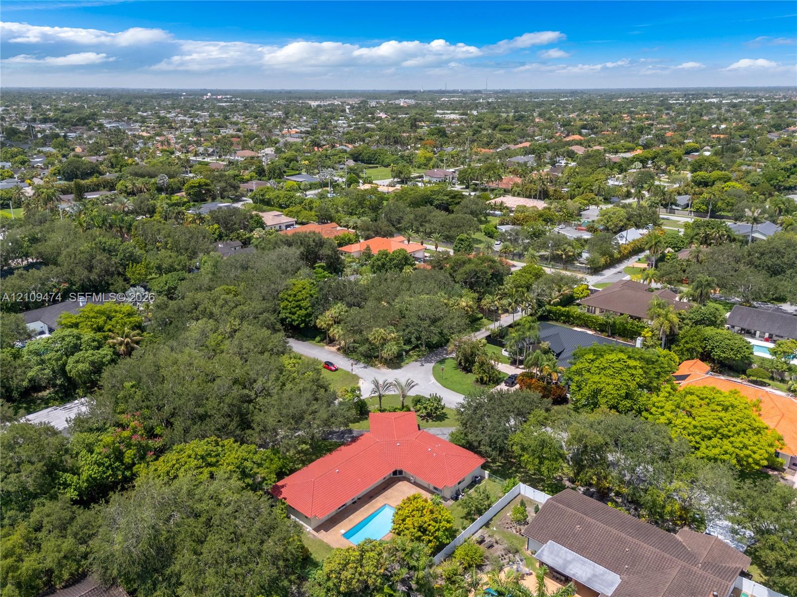 Aerial perspective featuring a property with a red-tiled roof, an integrated swimming pool, and mature trees situated on a spacious lot
