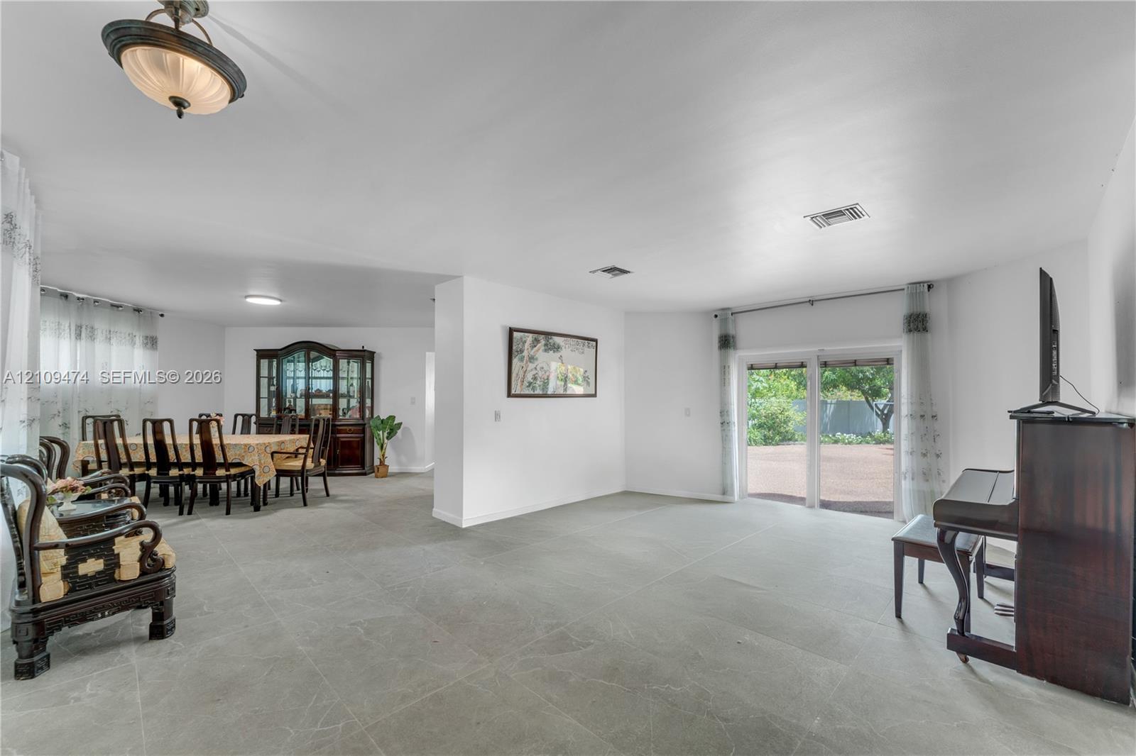 Open-concept interior featuring large-format tile flooring, sliding glass doors, neutral wall color, and a semi-flush mount light fixture