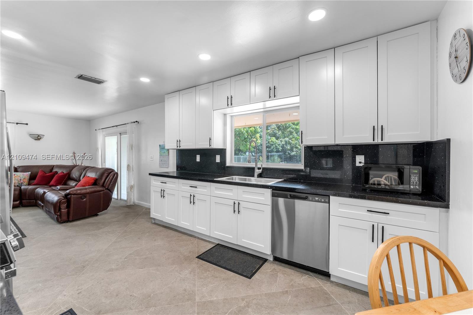 Kitchen featuring white shaker-style cabinetry, dark stone countertops, stainless steel dishwasher, and tile flooring