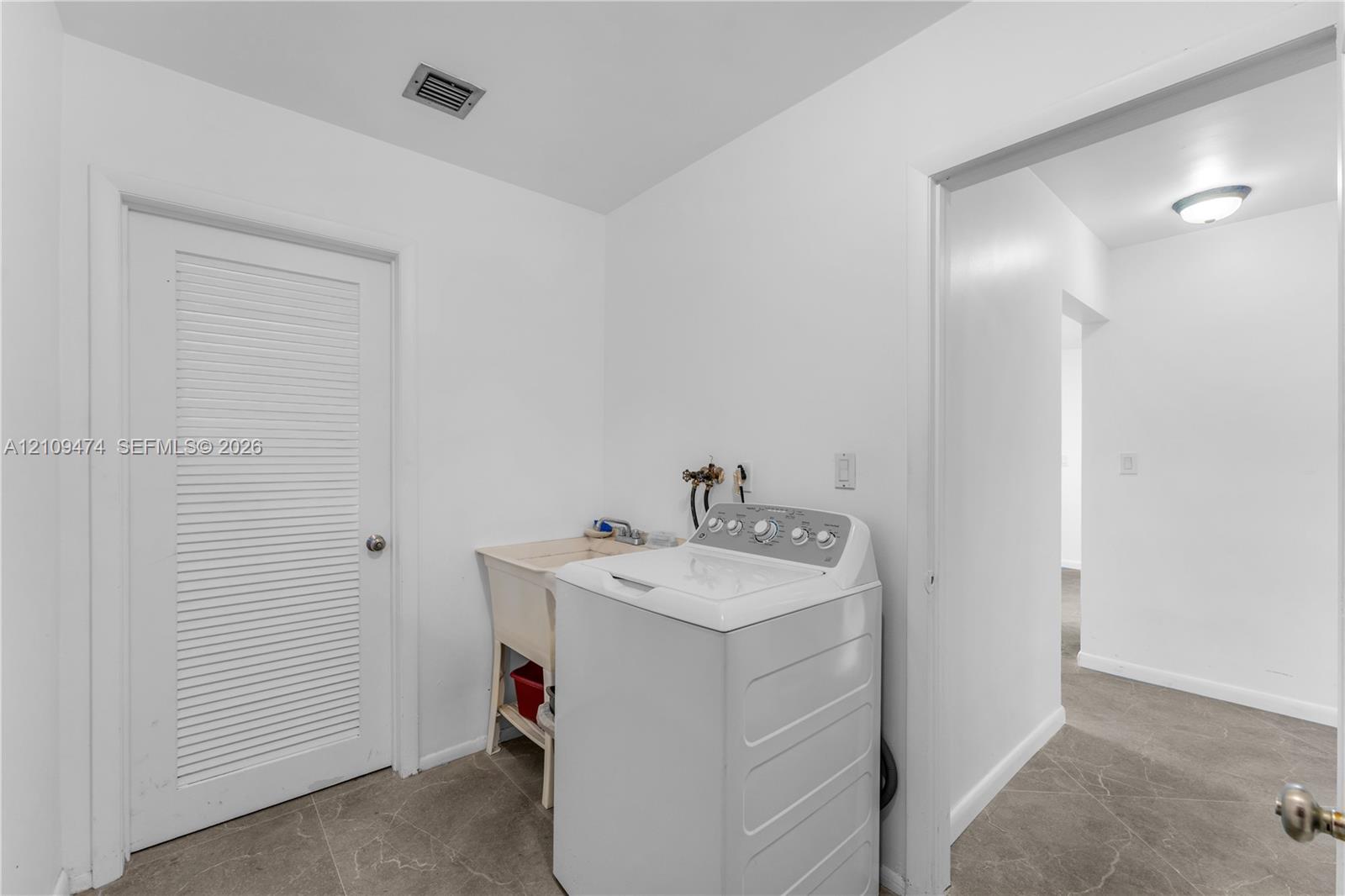 Utility space featuring tile flooring, a louvered door, a built-in basin sink, and washer hookups