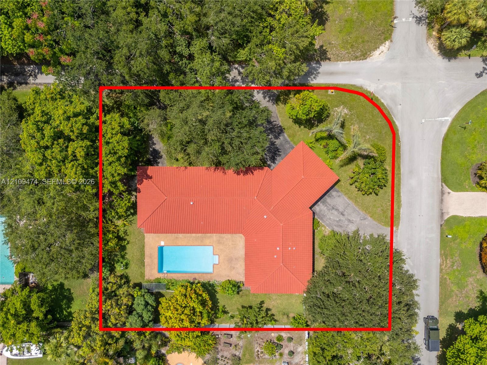 Corner lot featuring a red tile roof, inground swimming pool, paved patio, and mature tree canopy