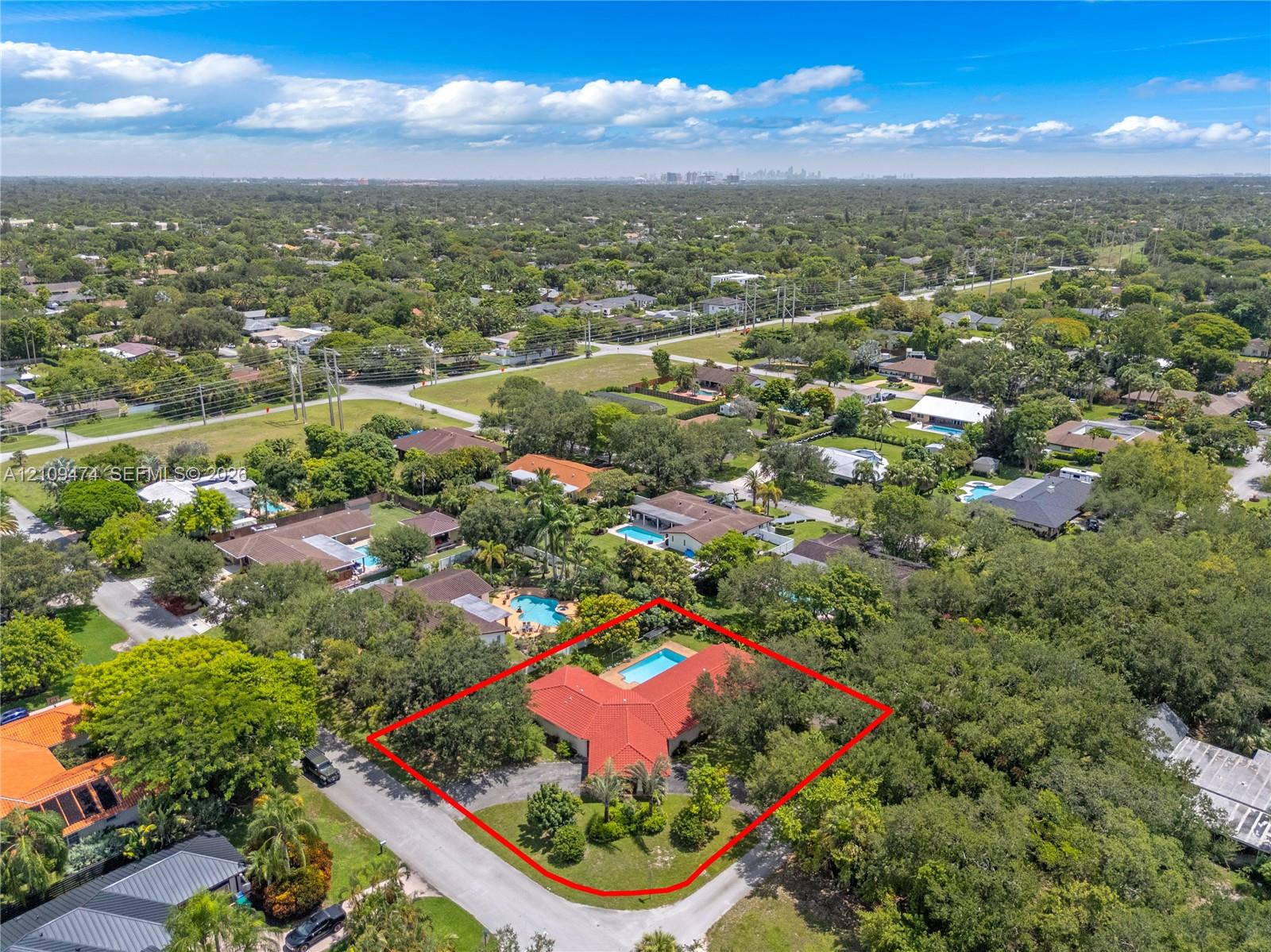 Aerial perspective featuring a red tile roof, an in-ground swimming pool, a sprawling lot with mature trees, and a concrete driveway