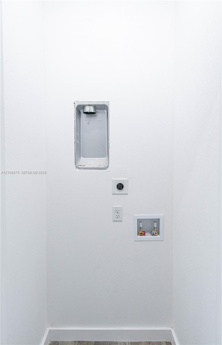 Utility hookup area featuring a recessed dryer vent box, dedicated 240-volt electrical outlet, standard electrical receptacle, and a recessed water supply valve box
