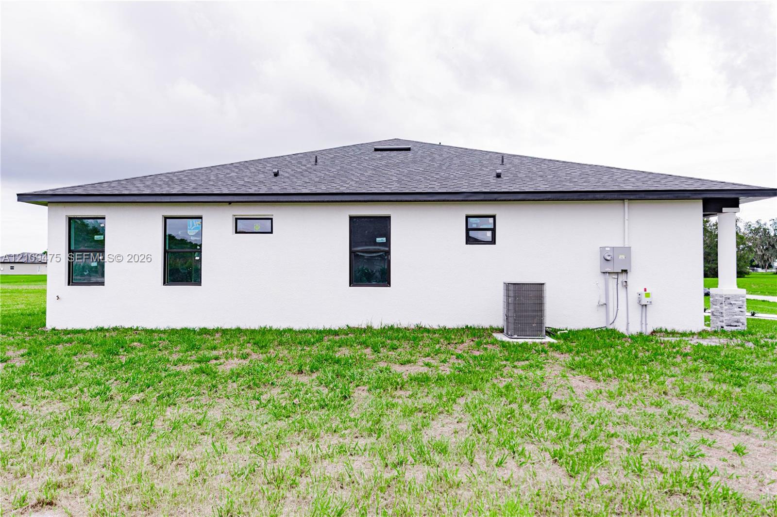 Stucco exterior featuring dark-framed windows, a hipped shingle roof, and stone-accented pillar
