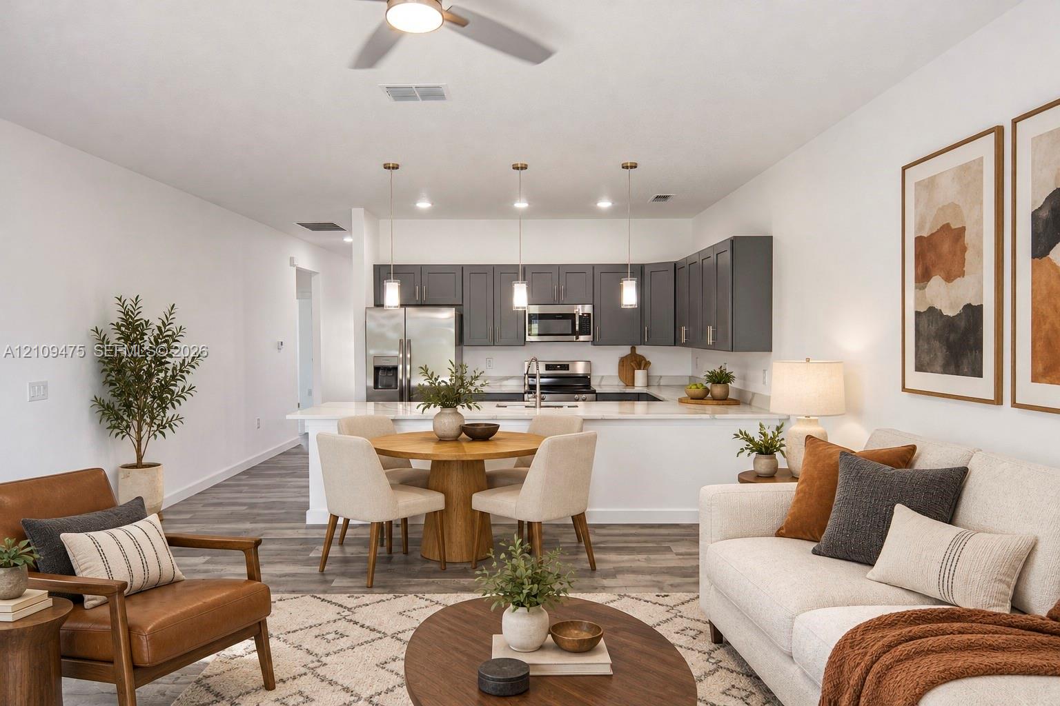 Open-concept kitchen featuring charcoal-toned cabinetry, stainless steel appliances, quartz countertops, a breakfast bar, and wood-finish flooring