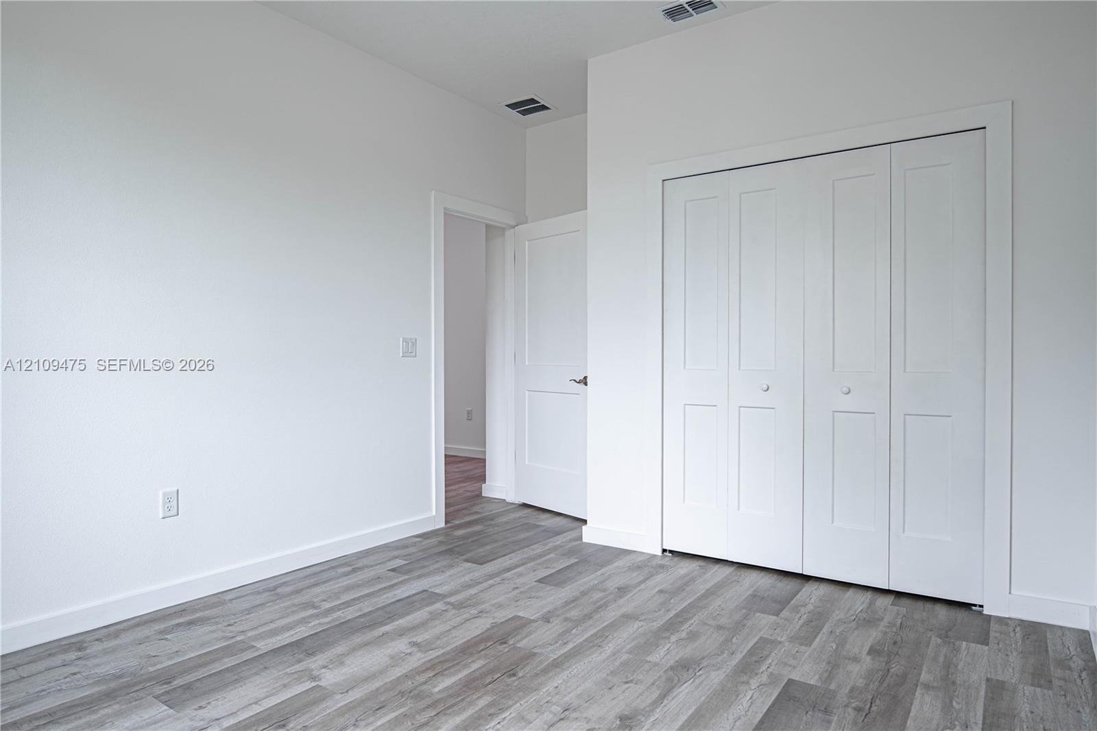 Room featuring wood-finish flooring, multi-panel bi-fold closet doors, and solid-core interior doors