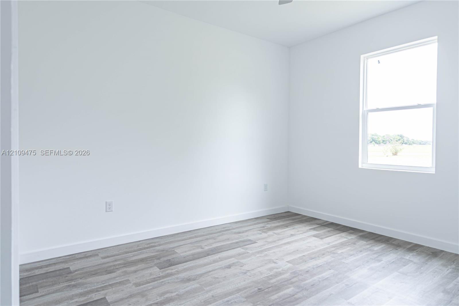Neutral-toned interior space featuring crisp white walls, wood-finish flooring, and a single-hung window