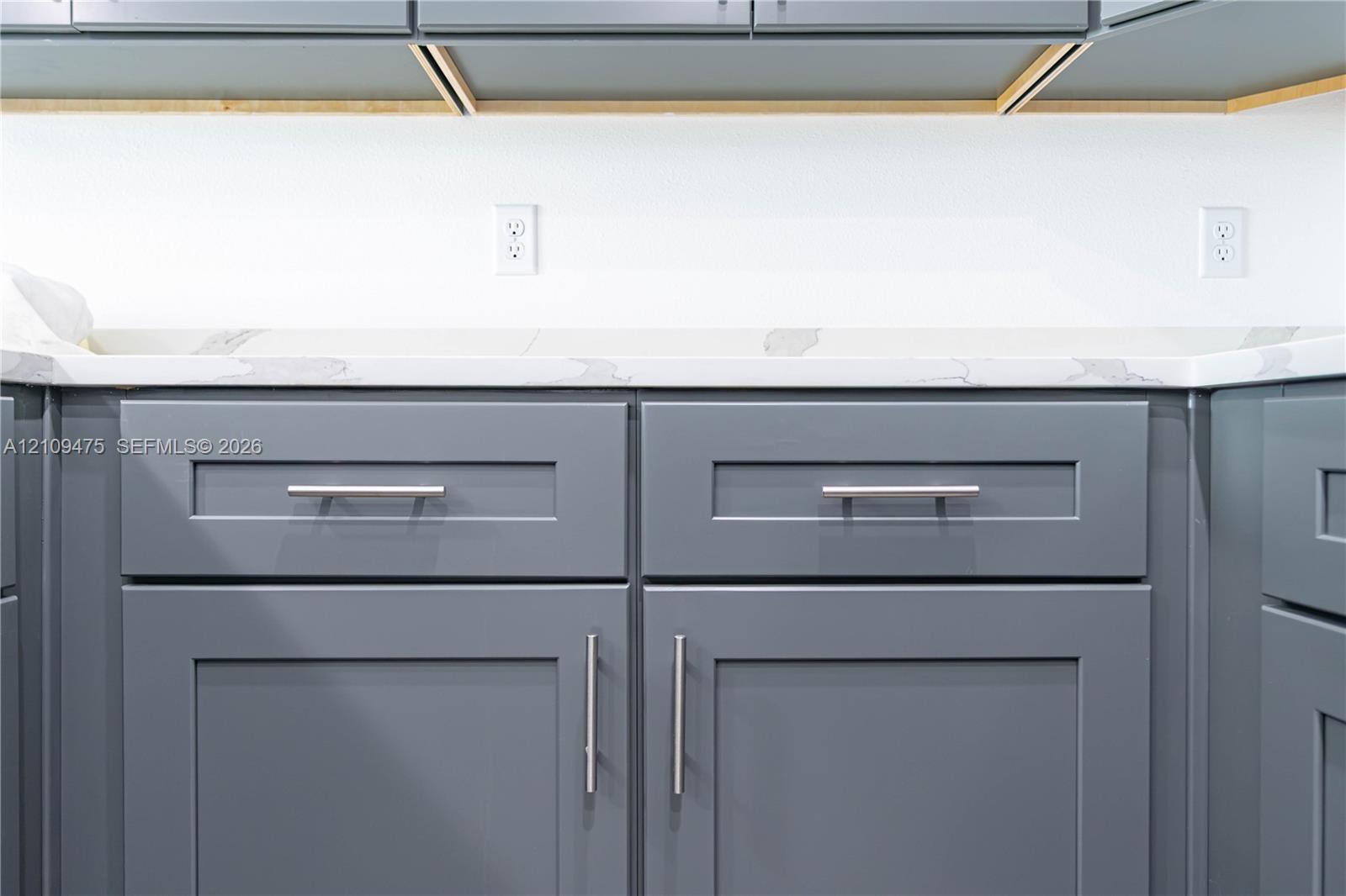 Shaker-style cabinetry finished in a slate grey tone, paired with a white stone-composite countertop featuring grey veining and brushed nickel hardware