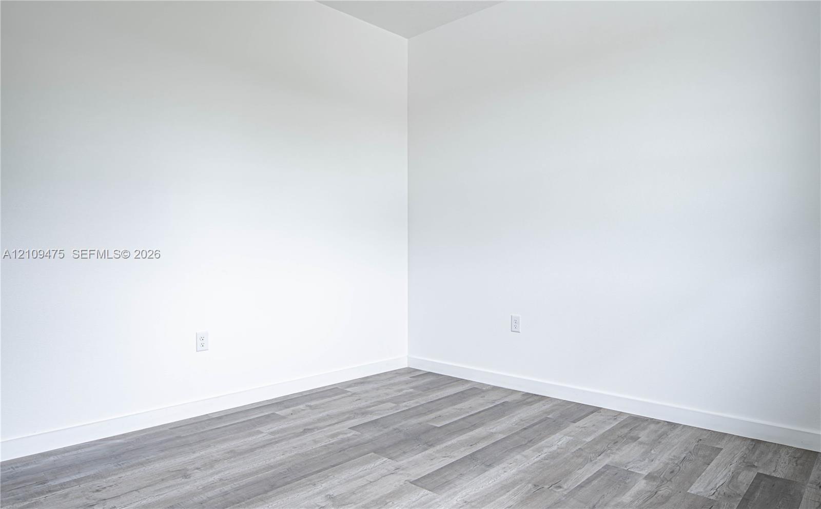 Neutral interior corner featuring smooth white walls and grey wood-finish flooring