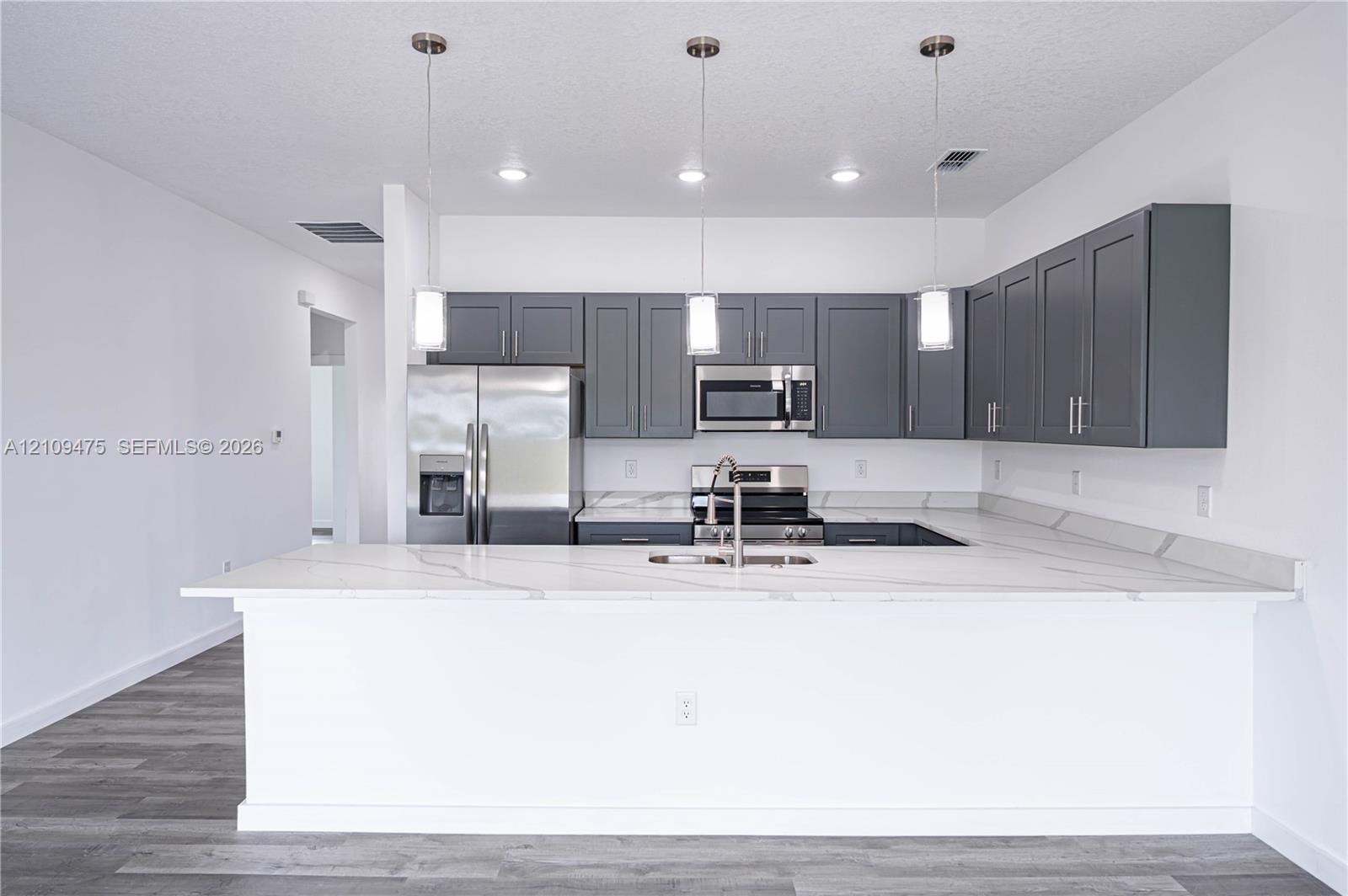 Kitchen featuring gray shaker-style cabinetry, a stone-finish island countertop, stainless steel appliances, and pendant lighting