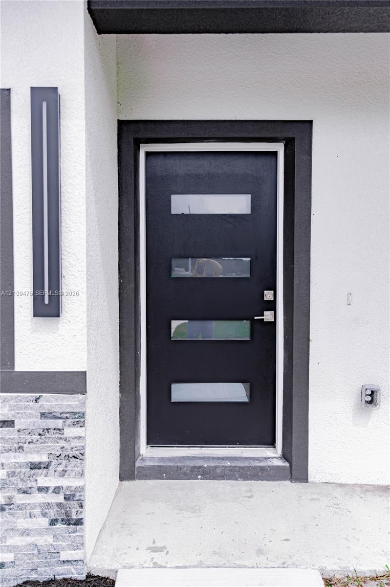 Modern black entry door featuring four horizontal glass inserts, brushed metal hardware, linear wall-mounted exterior lighting, and textured stone masonry detailing