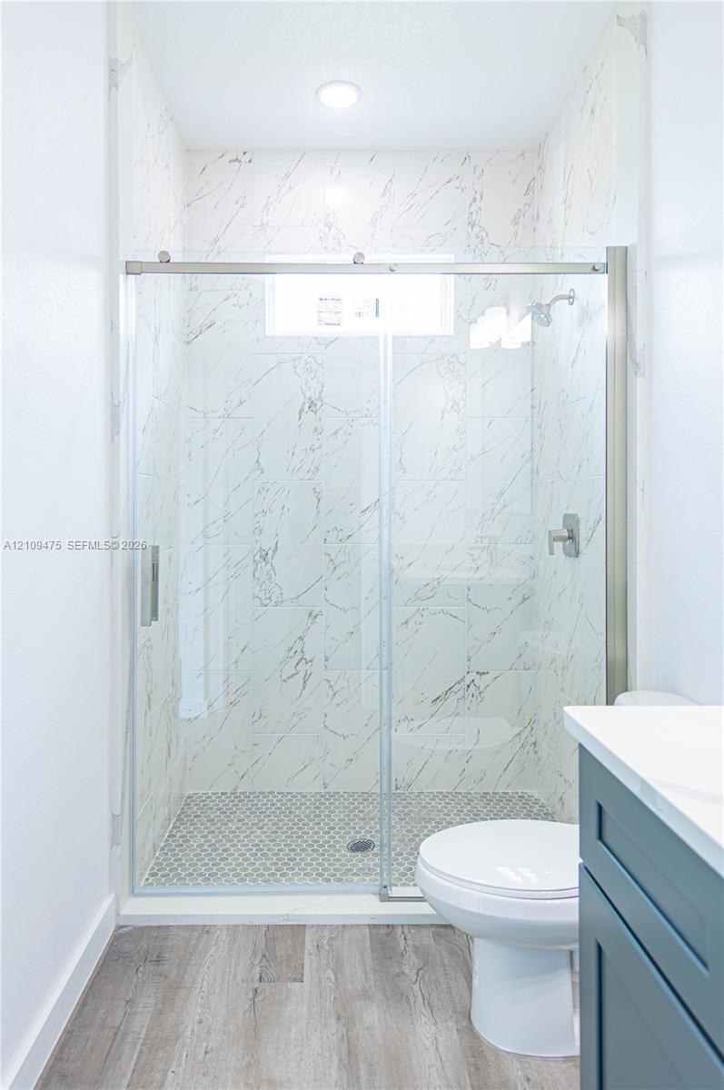 Walk-in shower featuring floor-to-ceiling stone-pattern tile, a sliding glass door, and a recessed ceiling light, accented by a dark-finish vanity cabinet and wood-finish flooring
