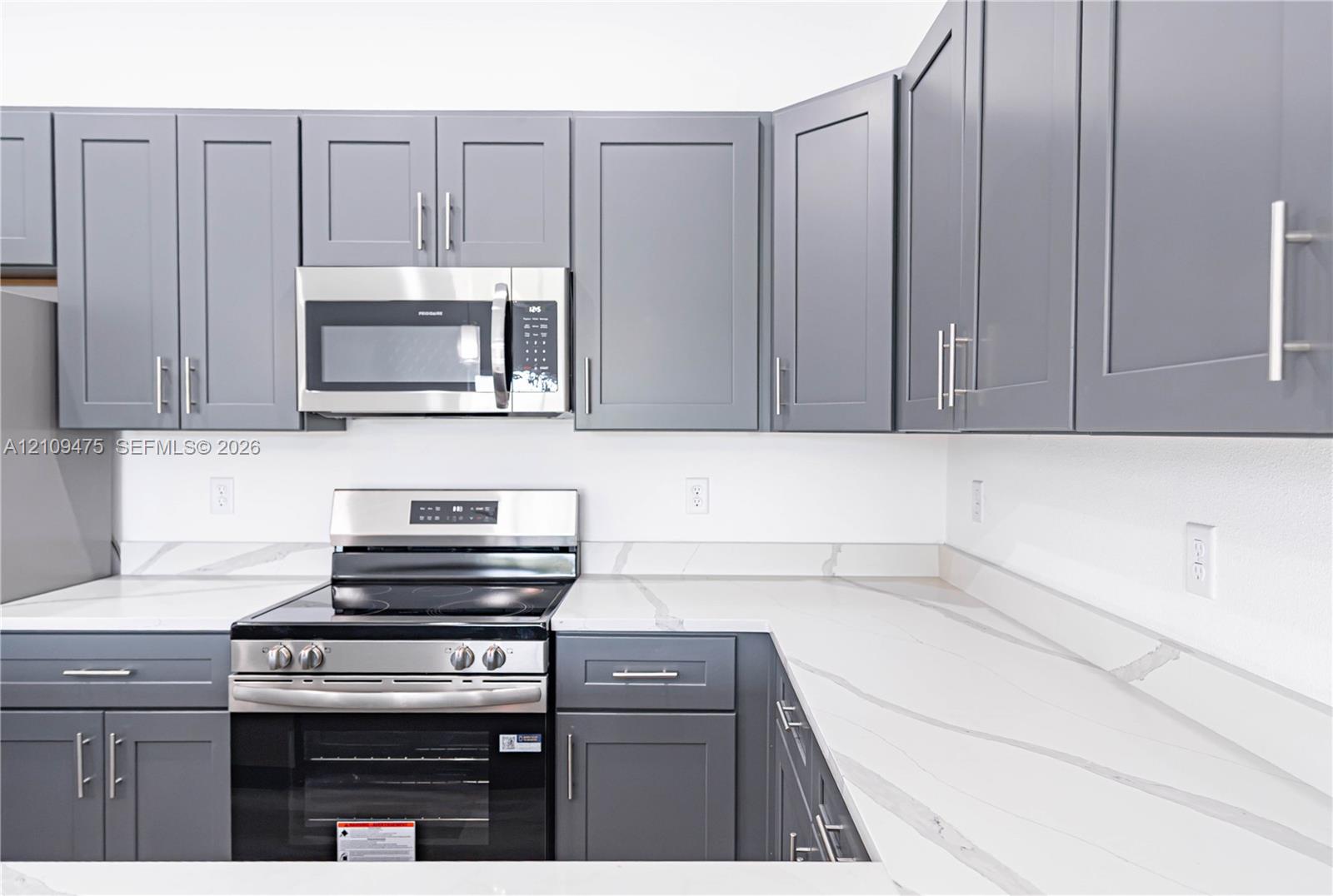 Kitchen featuring grey Shaker-style cabinetry, white countertops with integrated backsplash, and stainless steel appliances including a built-in microwave and range