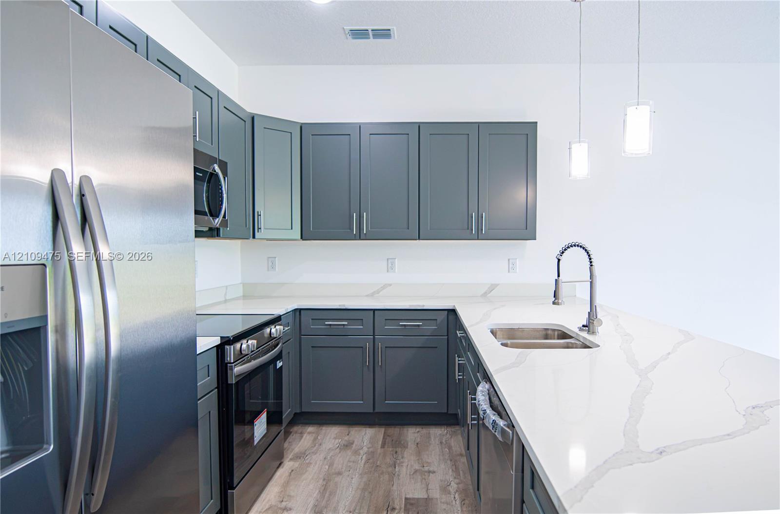 Kitchen featuring dark grey shaker-style cabinetry, white countertops with veining, stainless steel appliances, wood-finish flooring, and dual hanging pendant lights
