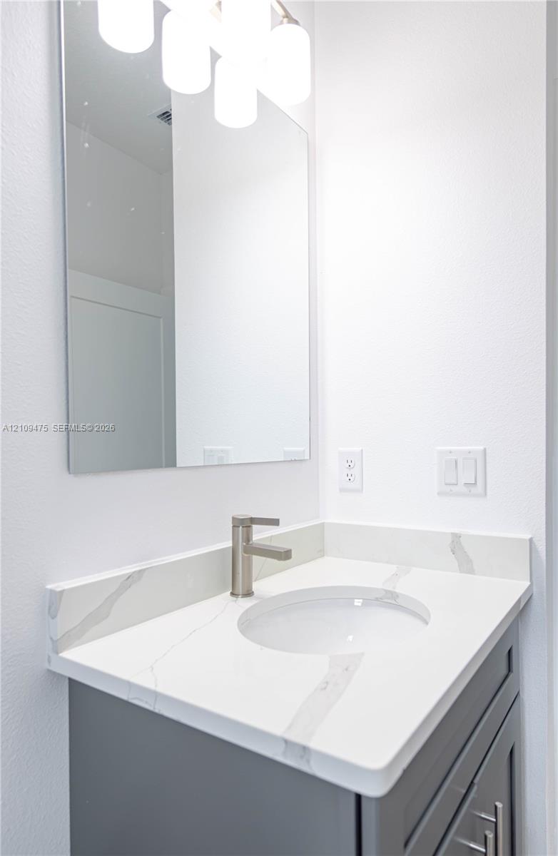 Vanity featuring a grey cabinet, white stone countertop with grey veining, integrated basin, brushed metal faucet, and a frameless wall mirror