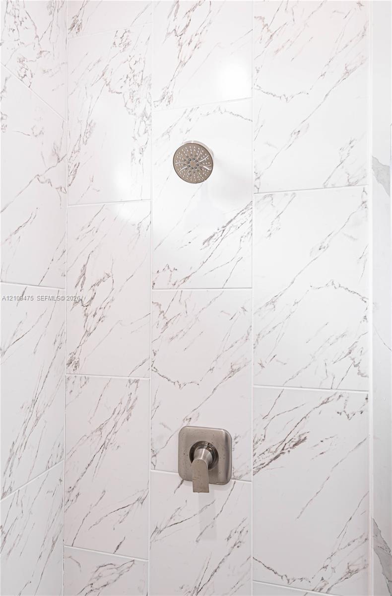 Shower enclosure featuring large-format veined tile walls, a brushed nickel rainfall showerhead, and a matching single-handle pressure-balance valve
