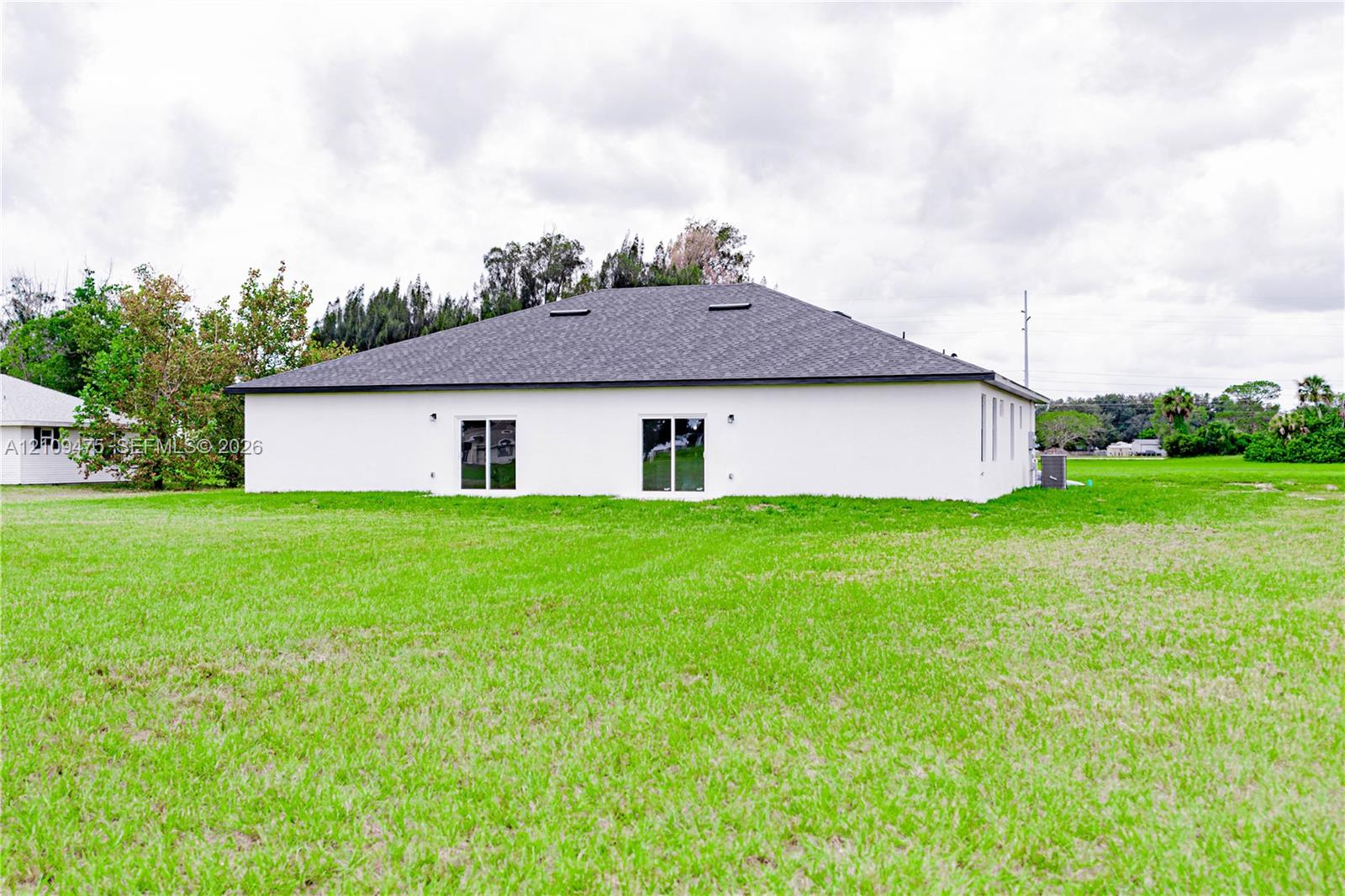 Single-story exterior featuring a white stucco facade, hip roof with integrated skylights, and two sliding glass doors opening to a large, open grass lot