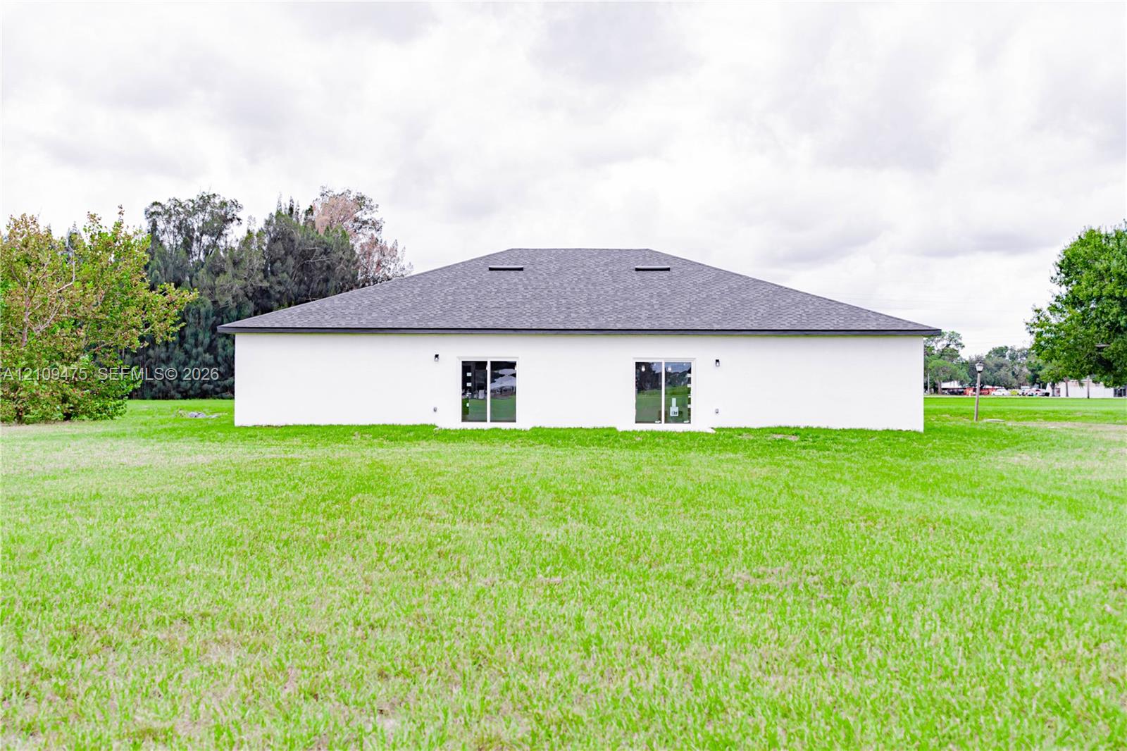 Exterior elevation featuring a light-toned smooth finish, hip roof with dark shingles, and dual glass sliding doors opening to an expansive grass yard