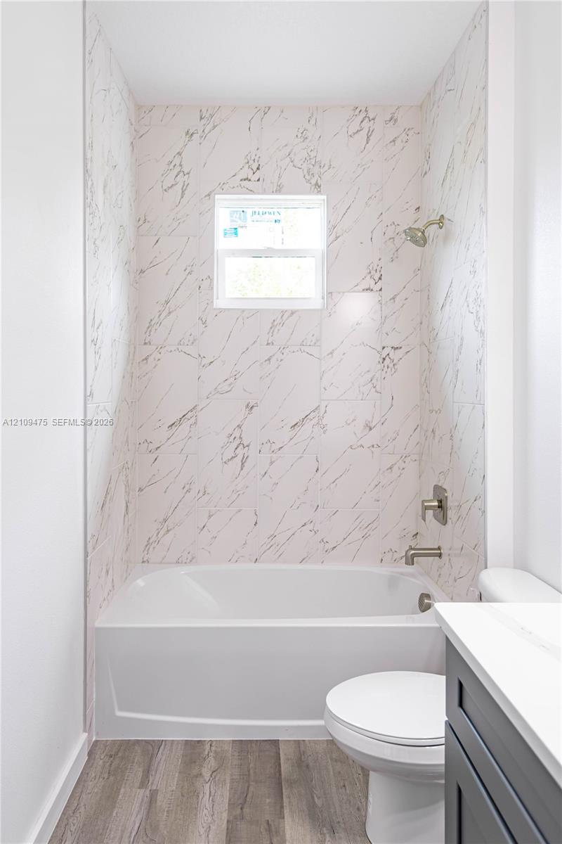Full-height tiled shower surround with veined pattern, integrated soaking tub, brushed nickel plumbing fixtures, inset window, and wood-finish flooring