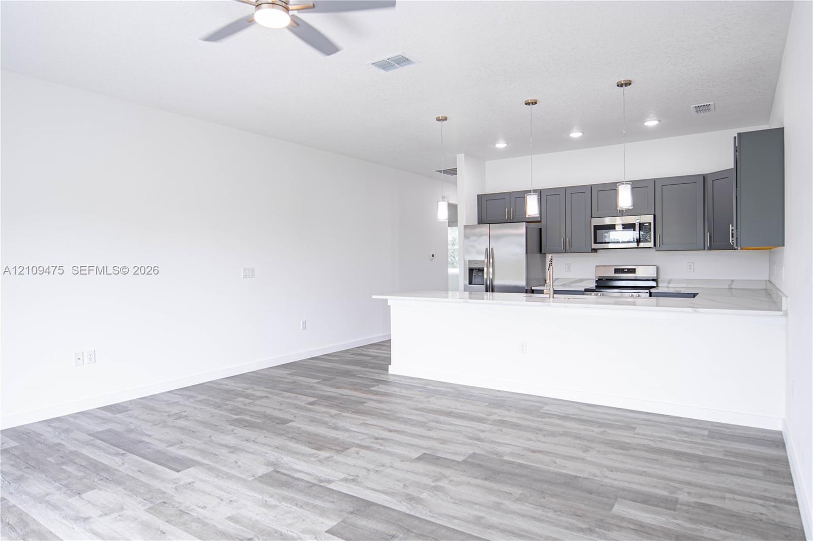 Kitchen featuring dark gray cabinetry, stainless steel appliances, a peninsula with stone-finish countertops, pendant lighting, and wood-finish flooring