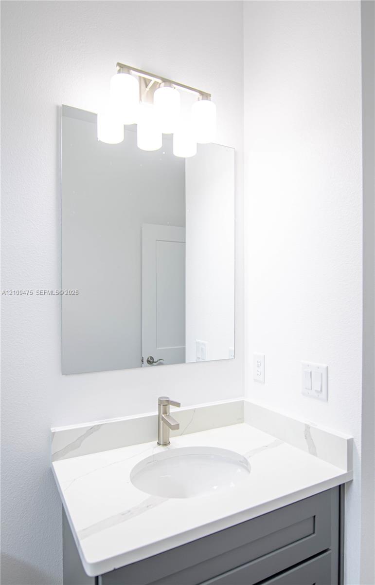 Vanity with a white surface featuring grey veining, integrated basin, grey cabinetry, wall-mounted mirror, and multi-bulb light fixture