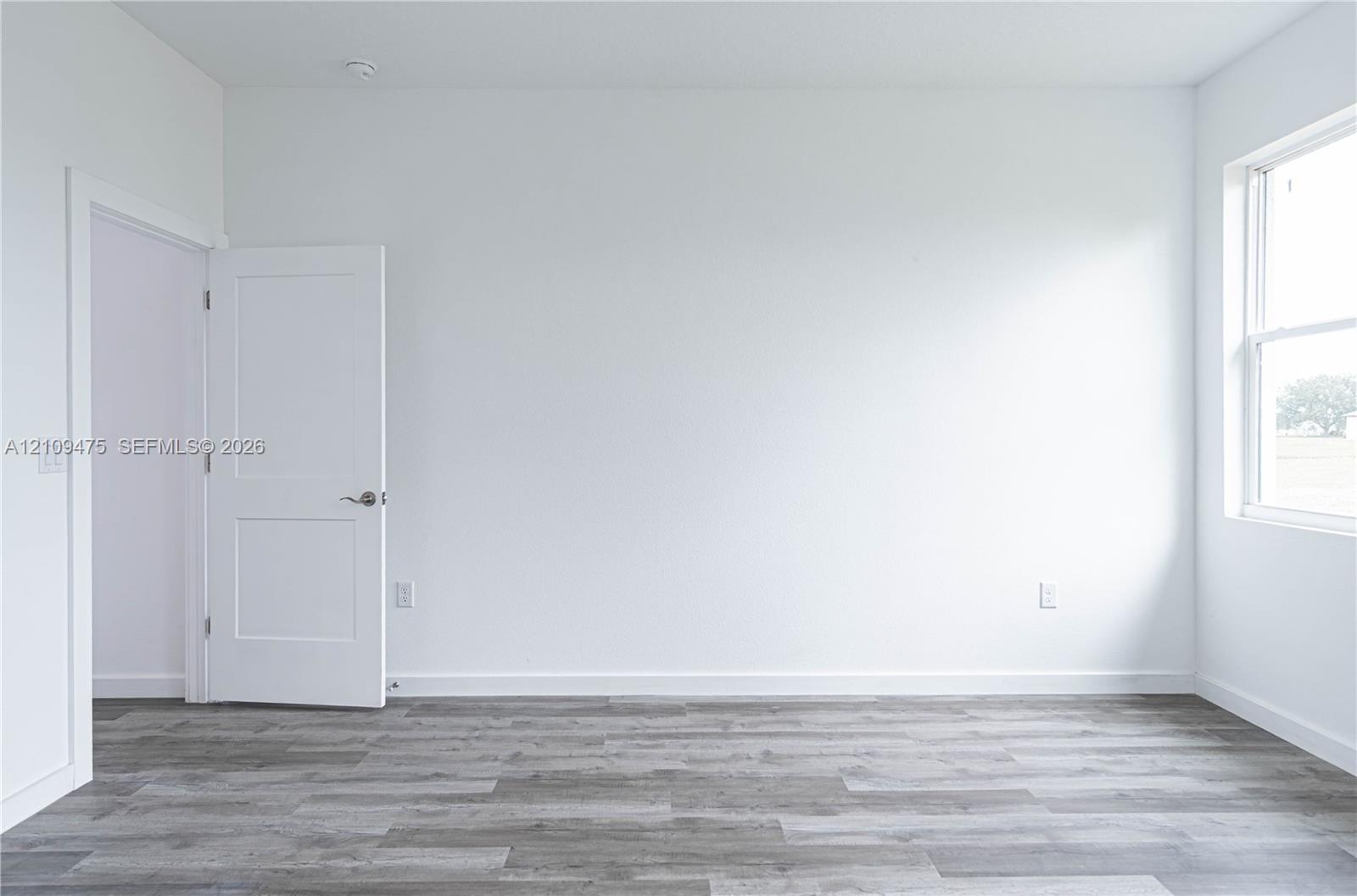 Interior room featuring wood-finish flooring, two-panel shaker style door, and a single-hung window