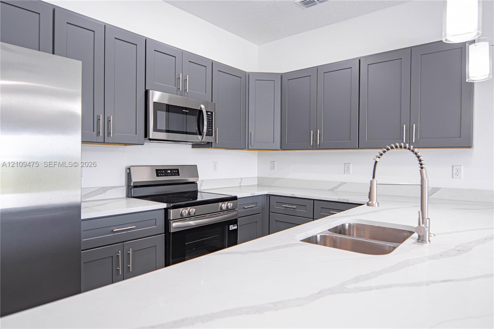 Kitchen featuring gray shaker-style cabinetry, white countertops with gray veining, stainless steel appliances, a double-basin undermount sink with a gooseneck faucet, and pendant lighting